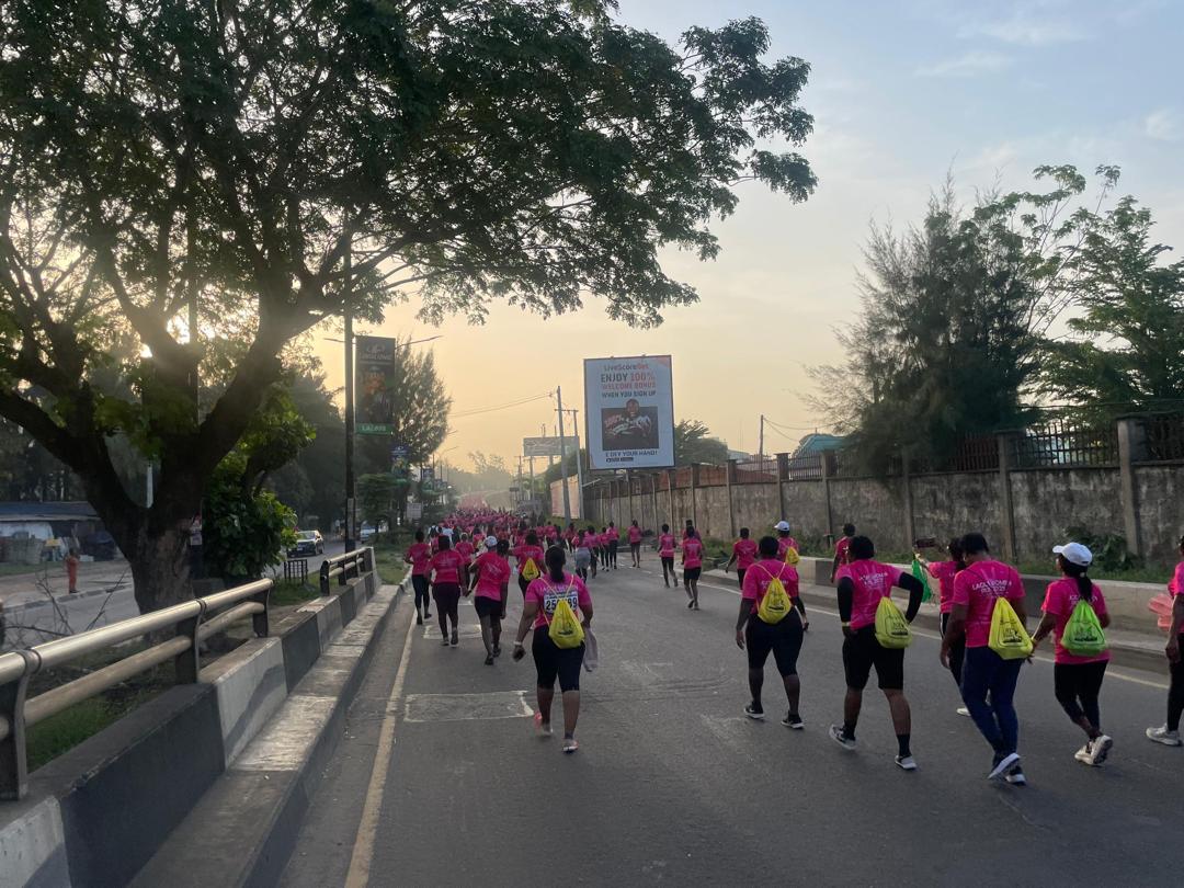 Runners in pink shirts on a tree-lined road in the early morning light